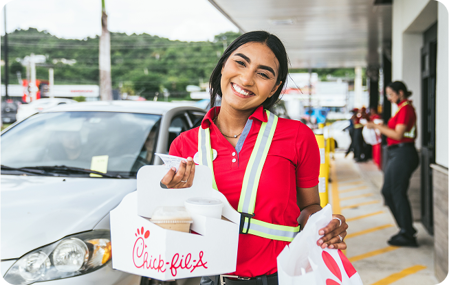 Team Member de pie afuera de un Restaurante con bebidas en un portavasos y una bolsa de comida de Chick-fil-A  