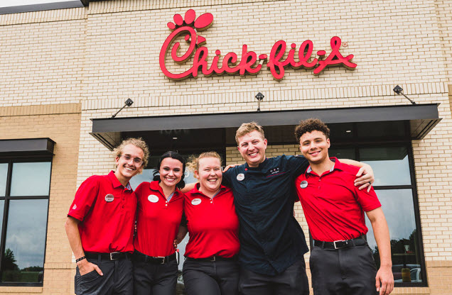 Cinco miembros del equipo de pie juntos afuera de un restaurante Chick-fil-A