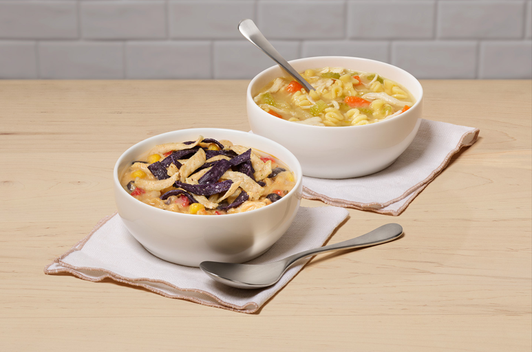 Boles de Chicken Tortilla Soup y de Chicken Noodle Soup sobre servilletas de tela en un fondoblanco