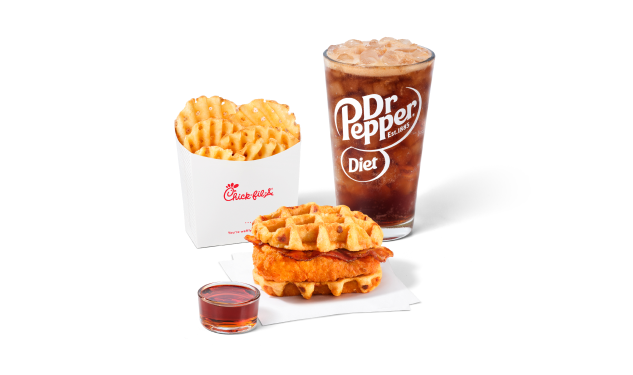Chicken & Waffles Sandwich servido sobre servilletas, con una porción de syrup clásico al lado, acompañado de Papas Fritas Waffle y una Coca-Cola® Zero Sugar